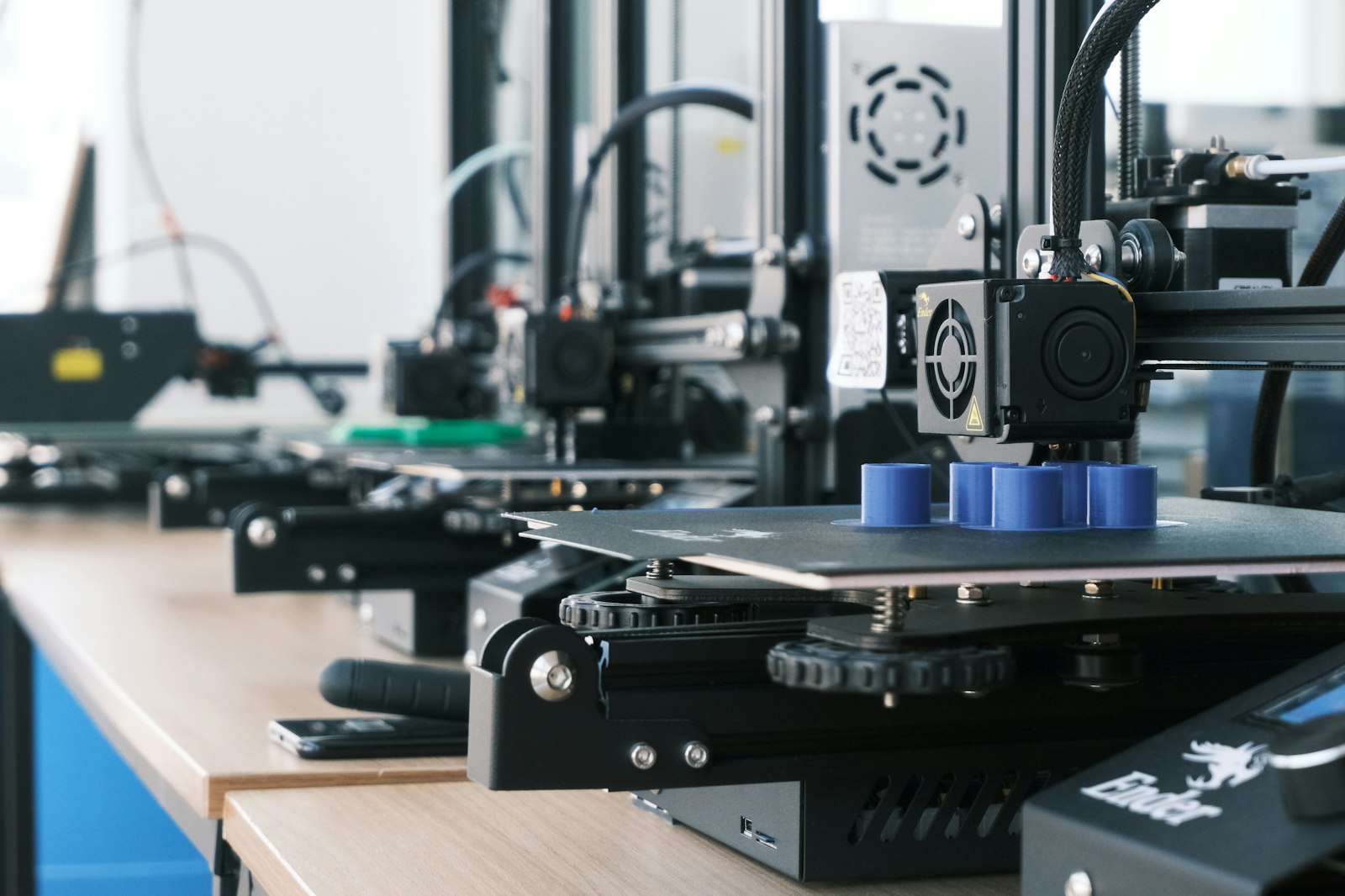 Row of 3D printers producing prototype parts on a workshop bench