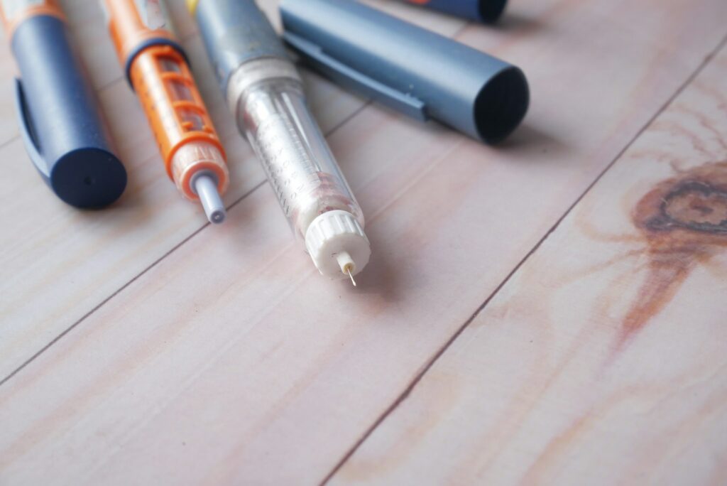Several insulin injection pens and a prefilled pen with needle attached, lying on a wooden surface