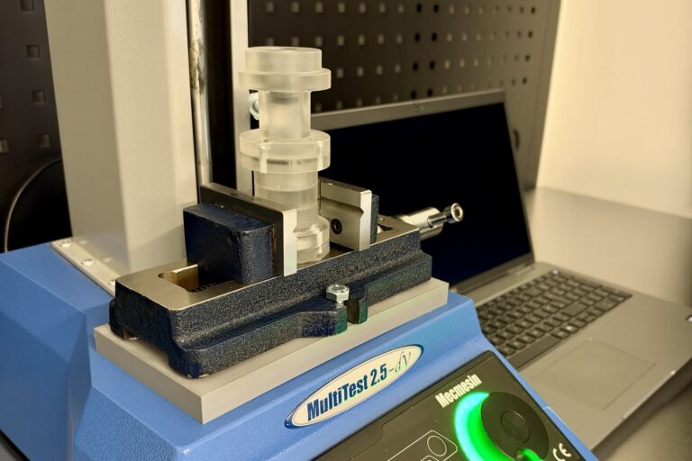 Close-up of a machined test specimen clamped in the vice of the Mecmesin MultiTest 2.5-dV force tester in the MDIN workshop