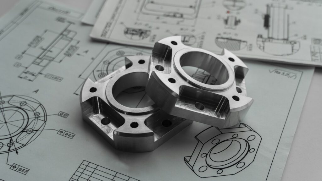 Two machined metal parts resting on printed engineering drawings