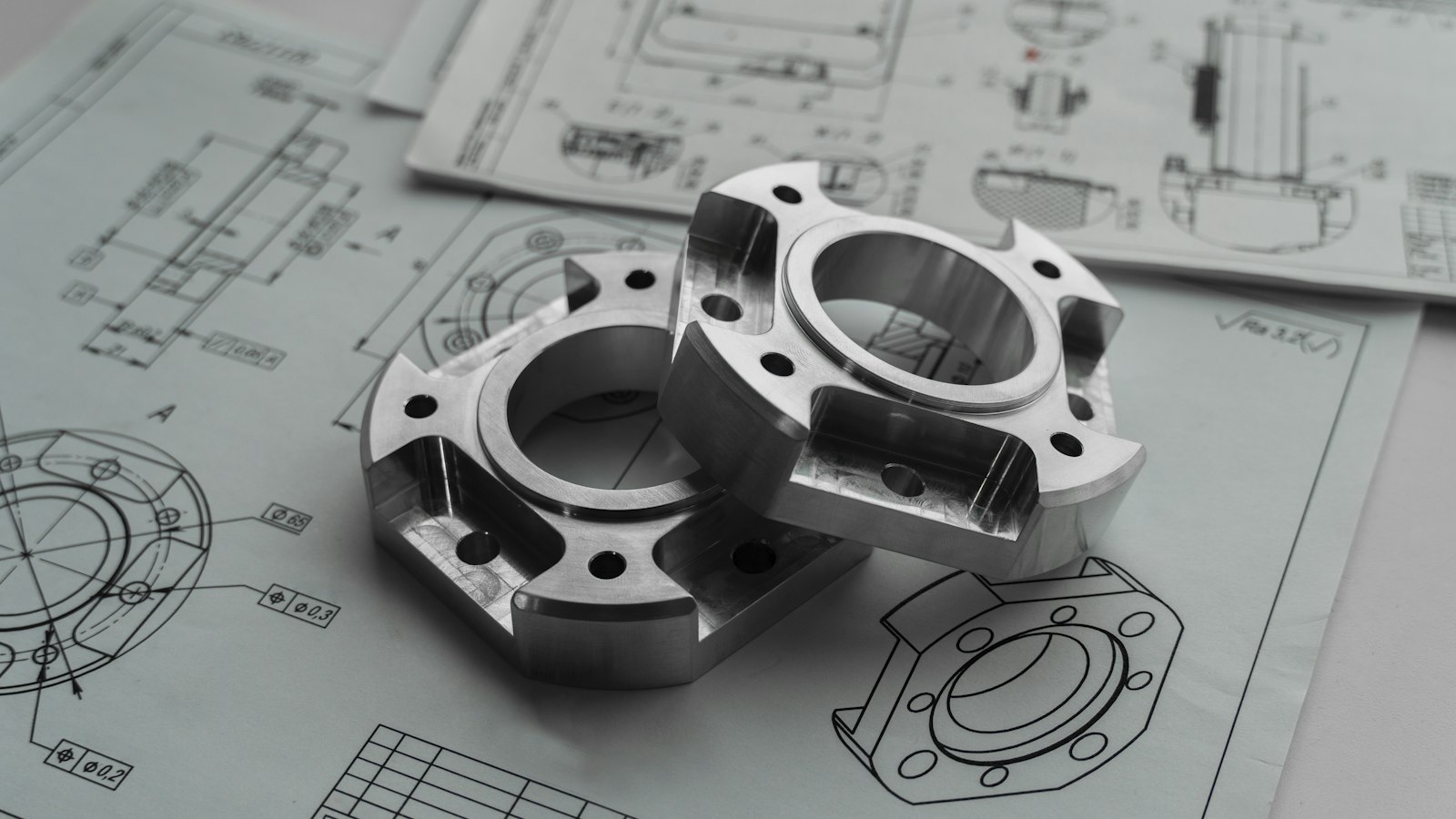 Two machined metal parts resting on printed engineering drawings